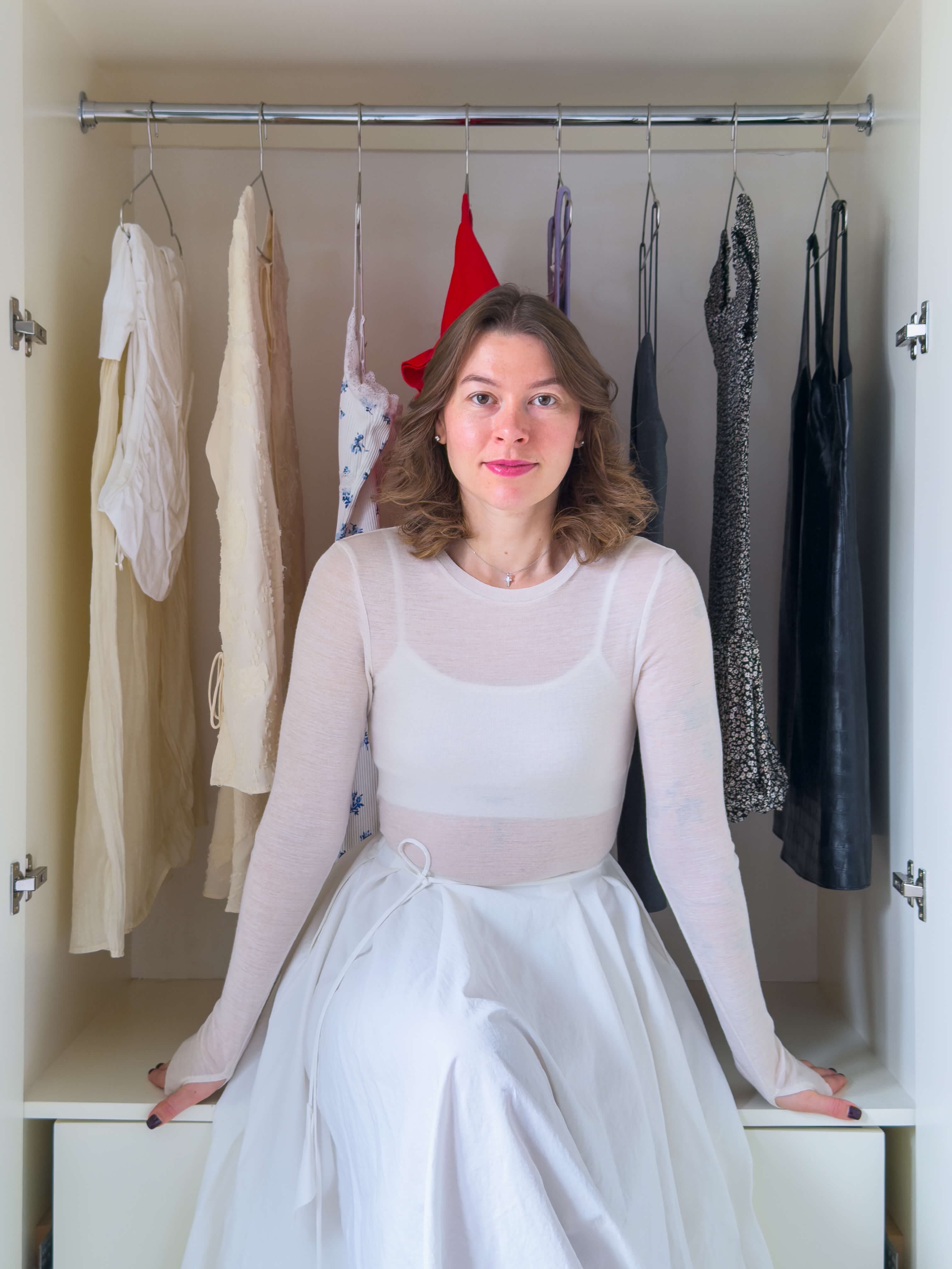 Maryna Kychka, professional home organiser in London, sitting inside a neatly organised wardrobe